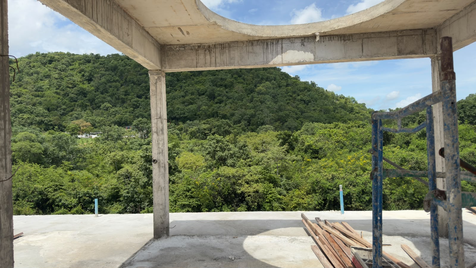 Rooftop terrace under construction with a circular roof opening framing views of the surrounding green hills.